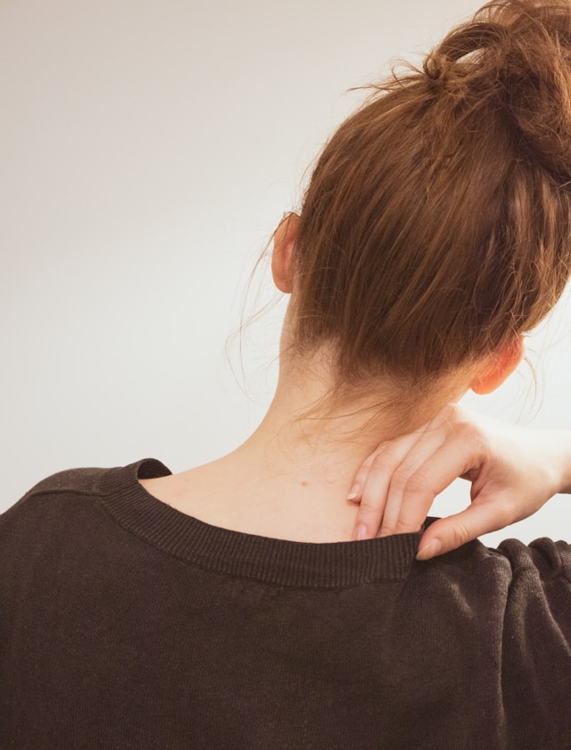 Person holding the back of their neck with tension and pain